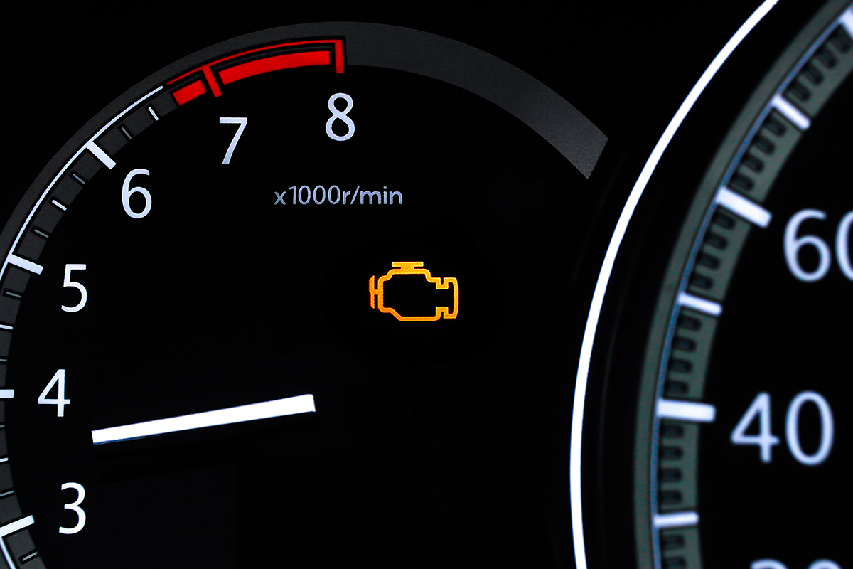 Check engine light or warning light closeup, Closeup of a car dashboard with an illuminated check engine light and the tachometer displaying engine revolutions per minute.